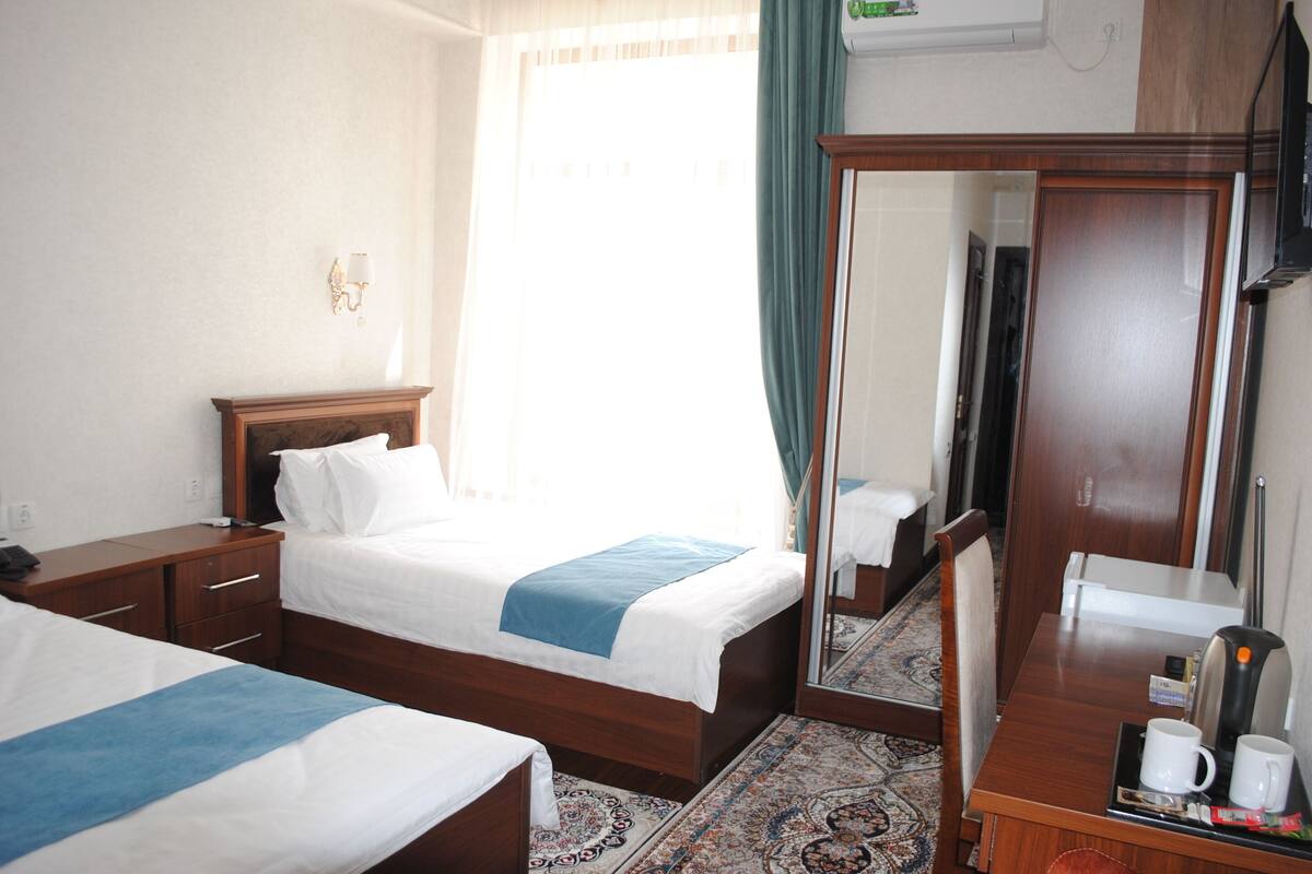 Quarto de hotel com duas camas, um guarda-roupa de madeira, um espelho, uma máquina de café e uma mesinha com bandeja.