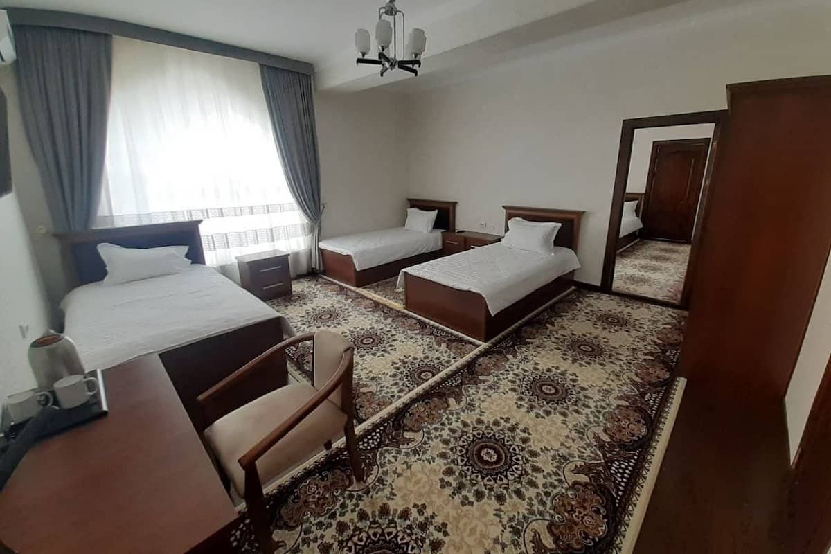 Quarto de hotel com duas camas de solteiro, uma escrivaninha, uma cadeira, uma mesinha com uma chávena e um tapete estampado.