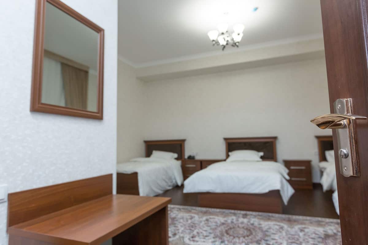 Quarto de hotel com duas camas, um banco de madeira, um espelho e um lustre.
