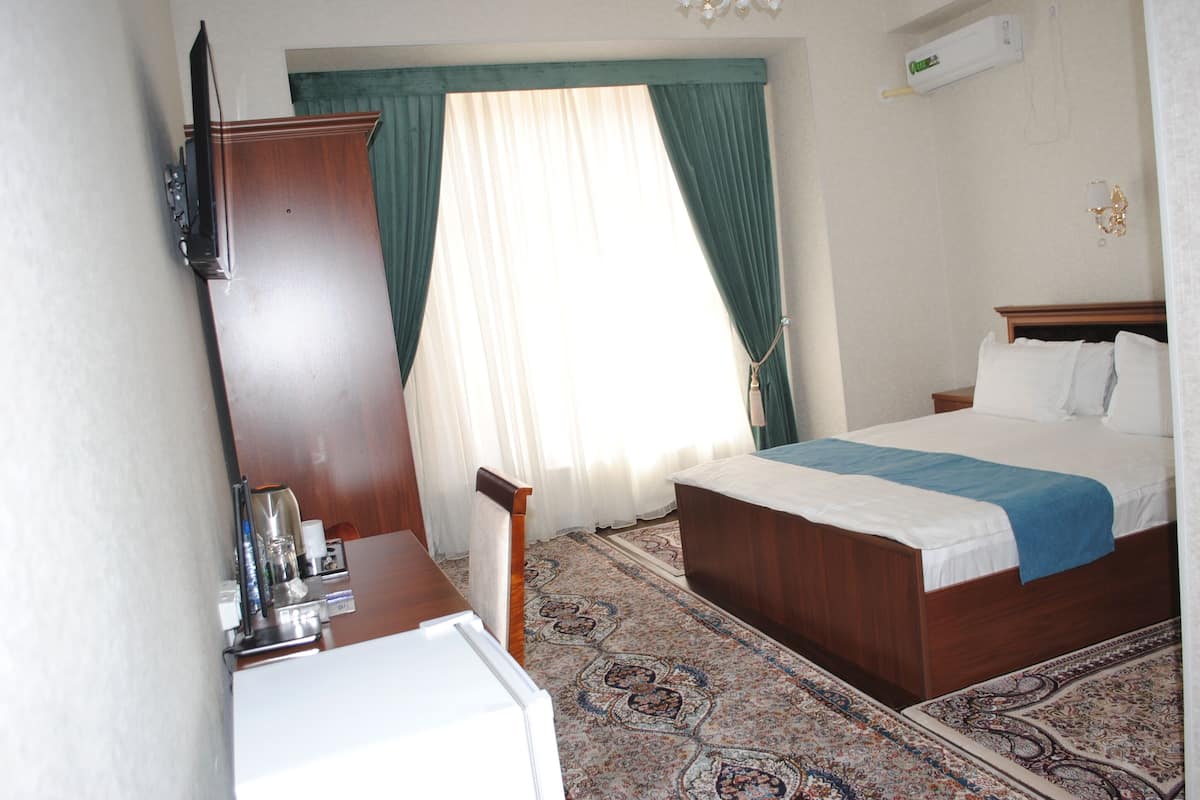 Quarto de hotel com cama, escrivaninha, cadeira, televisão e janela com cortinas.
