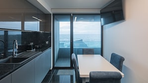 A compact kitchen with a view of the ocean, a dining area with a table and chairs, and a flat-screen TV mounted on the wall. - SeaLux Apartment - Seaside (Ponta Delgada)