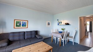 Een woonkamer met een bank, een salontafel, een eettafel met stoelen en ingekaderde foto's aan de muur.