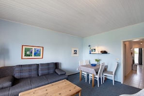 Un salon comprenant un canapé, une table basse, une table à manger avec des chaises et des tableaux encadrés accrochés au mur.