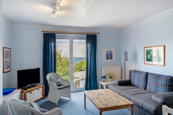Una sala de estar con televisión, sillas de mimbre, sofá, mesa y vistas a través de un ventanal.