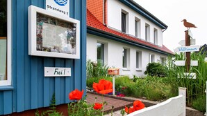 Een gebouw met een blauwe gevel, een bord met de tekst 'Strandweg 2' en een welkomstbord.