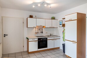 Una cocina compacta con armarios blancos, estufa, lavabo y refrigerador.