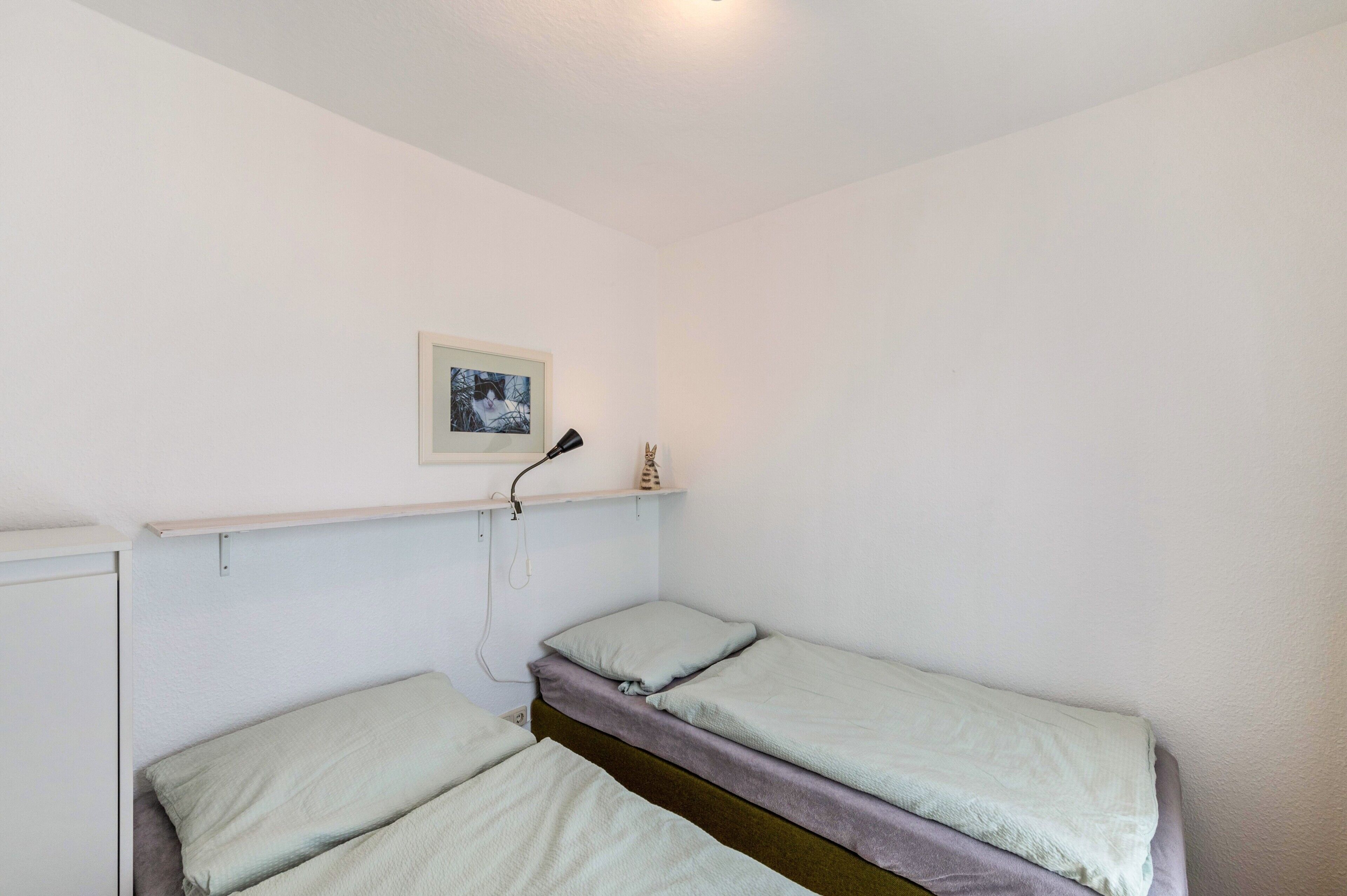 A small, single-room accommodation with two single beds, a shelf with a picture, and a power outlet.