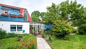 Una casa con techo rojo, fachada azul y jardín con flores rojas y un sendero.