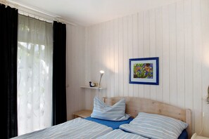 Quarto com cabeceira de madeira, cama com roupa de cama azul, mesa de cabeceira com abajur, prateleira com objeto decorativo e quadro na parede.