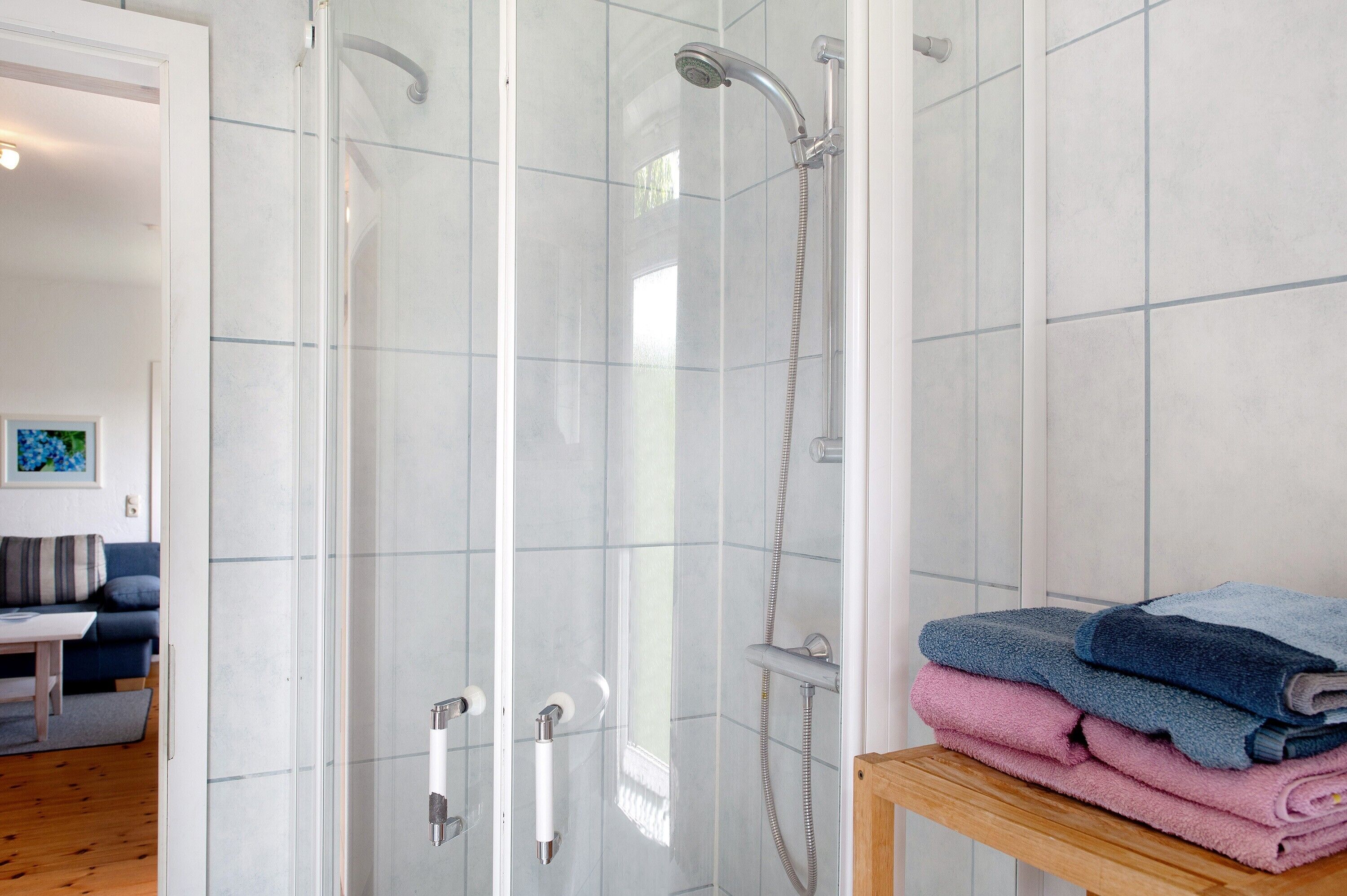 A glass-enclosed shower with a handheld showerhead, a towel rack with folded towels, and a wooden table.