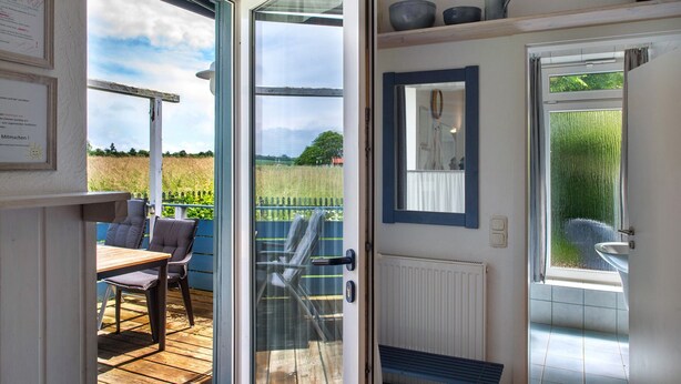 Une pièce dotée d’une terrasse en bois, d’une porte donnant sur une salle de bain et offrant une vue sur un jardin.