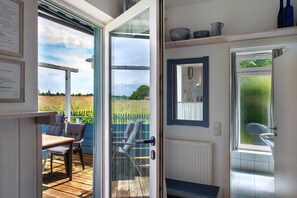 Une pièce dotée d’une terrasse en bois, d’une porte donnant sur une salle de bain et offrant une vue sur un jardin.