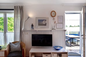 A living room with a television, a wicker chair, a blue bowl, and a framed picture on the wall. - Holiday Home 'Möve Aba Bungalow 68' with Private Terrace, Shared Garden and Wi-Fi (Rerik)