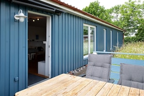 Um edifício azul com um deck de madeira e uma porta que dá para o interior.