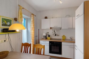 A compact kitchen with white cabinets, a stove, a sink, and a dining area with a table and chairs.