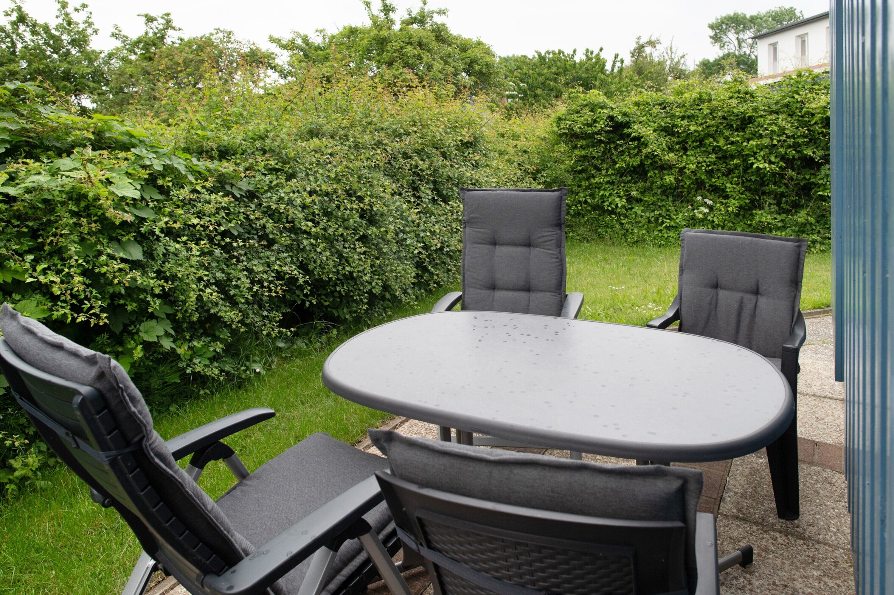 Eine Terrasse mit einem runden Tisch und vier Stühlen, umgeben von Pflanzen.