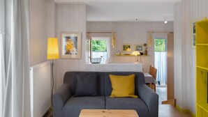 Un salon comprenant un canapé, une table basse en bois, un radiateur, une fenêtre avec des rideaux et une étagère jaune.