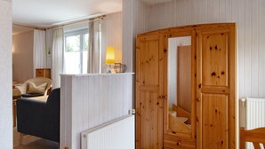 Une pièce comprenant un lit, une chaise, une armoire en bois, un radiateur et une fenêtre avec des rideaux.