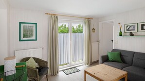 Una habitación con sofá, silla, mesa, radiador y ventana con cortinas.