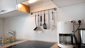 Una cocina con una estufa moderna, una cafetera y utensilios colgando en la pared.