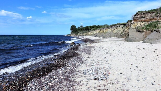Una playa de piedras, un acantilado rocoso y el océano.
