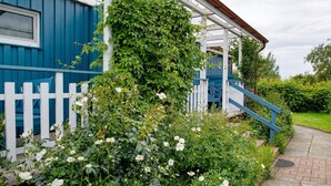 A blue building with a white picket fence, a covered porch, and a pathway leading to a blue staircase. - Holiday home "Möve ABA Bungalow 63" with private terrace and WLAN (Rerik)