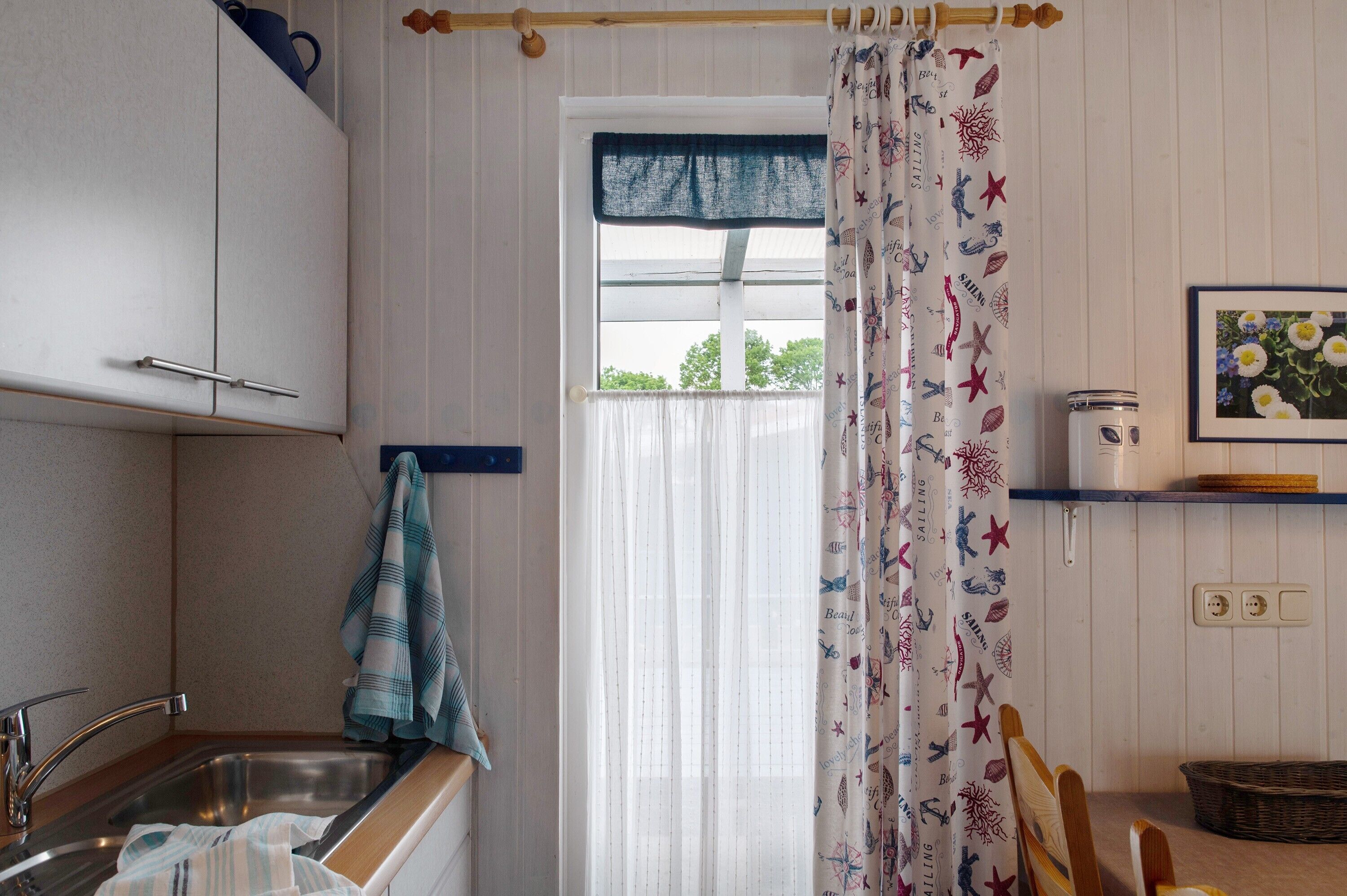 A kitchen with a sink, cabinets, a window with a curtain, and a shelf with a can and a basket.
