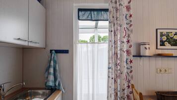 A kitchen with a sink, cabinets, a window with a curtain, and a shelf with a can and a basket.