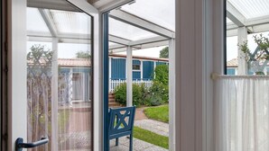 A covered outdoor area with a bench, a white door, and a view of a house with a blue fence. - Holiday home "Möve ABA Bungalow 62" with private terrace and WLAN (Rerik)