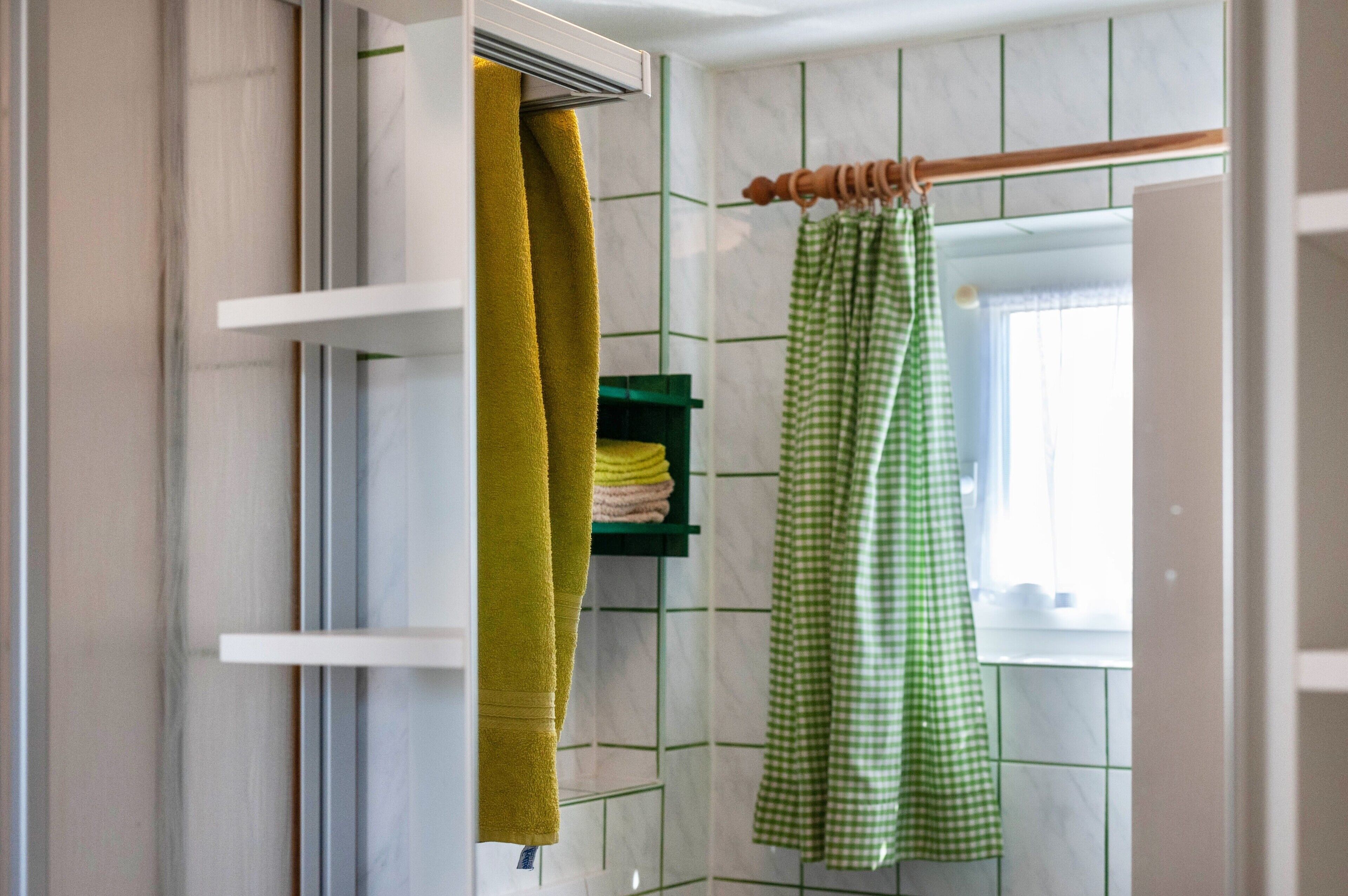 A bathroom with a towel rack, a green towel, and a green checkered bathrobe.