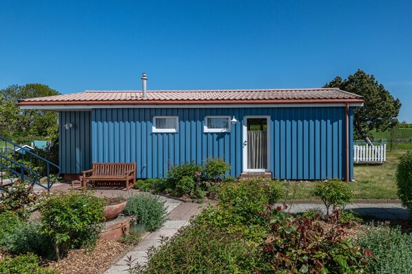 A small blue building with a red roof, a wooden bench, and a white fence in the background.