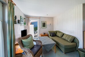 A cozy room with a wicker chair, a green sofa, a small table, and a television.