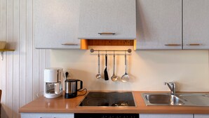 A kitchen with a built-in stove, a coffee maker, a kettle, and hanging utensils. - Holiday home "Möve ABA Bungalow 60" with private terrace and WLAN (Rerik)