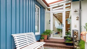 A white bench outside a building with blue siding, a door with glass panels, and a number '2' sign. - Holiday home "Möve ABA Bungalow 60" with private terrace and WLAN (Rerik)
