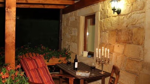 A wooden table with a bottle and glasses, a red-striped chair, and a stone wall with a window.