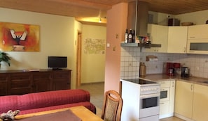 Une cuisine compacte équipée d’une cuisinière, d’un four à micro-ondes et de placards. On aperçoit un coin repas avec un canapé et une table rouges.