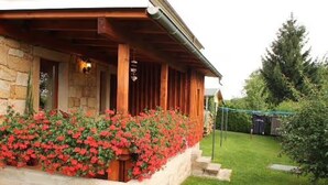 A stone building with a wooden porch, a flower bed with red flowers, and a green lawn.