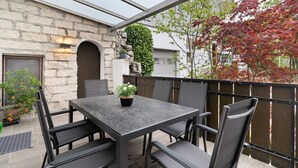 Un patio con una mesa y sillas, un muro de piedra y vistas a un edificio con un árbol.