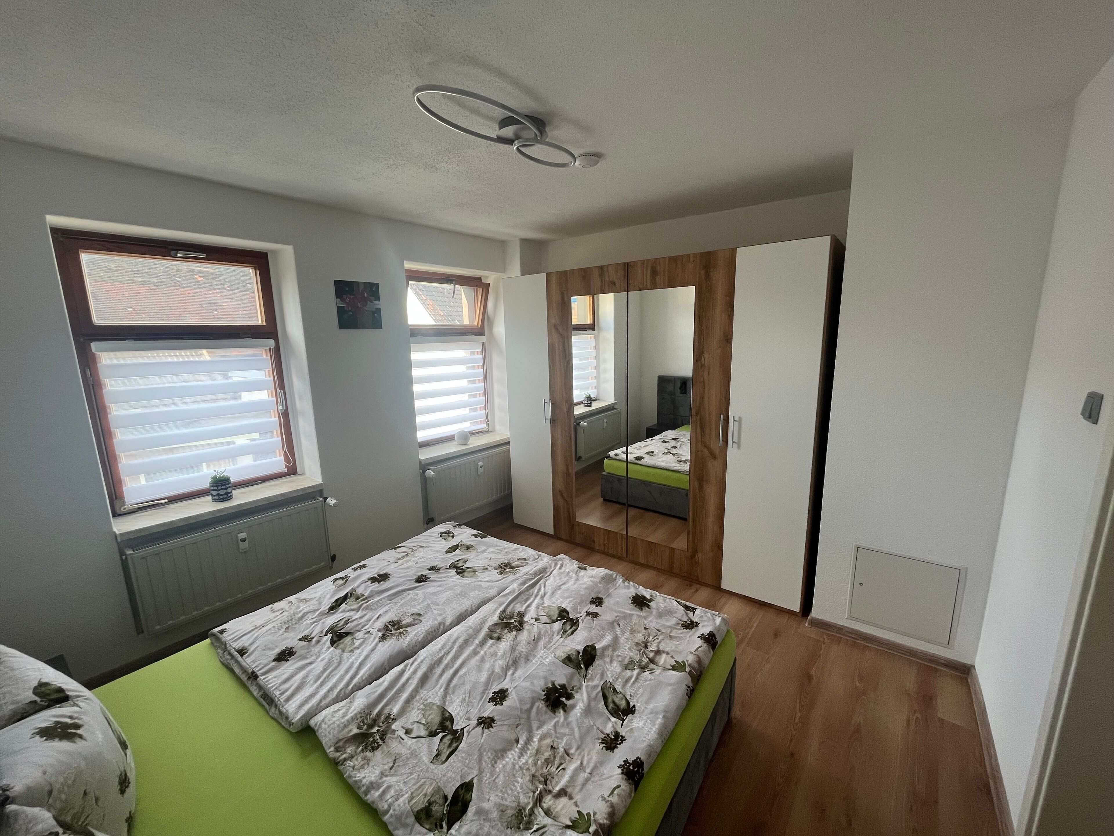 Une chambre à coucher comprenant un lit, une fenêtre, un radiateur, un ventilateur de plafond et un miroir.