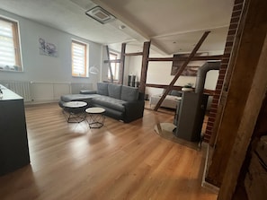 Ein modernes Wohnzimmer mit einer Eckcouch, zwei kleinen runden Tischen und einer Treppe, die in einen oberen Bereich führt.