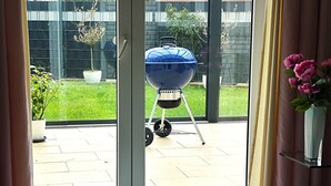 Una stanza con una porta a vetri scorrevoli che dà su un patio con una griglia per barbecue, piante in vaso e un vaso con fiori.