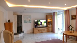 A modern living room with a flat-screen TV, a fireplace, a dining area, and a large window with curtains. - Holiday Home 'Grand Westfalia' with Terrace, Sports Room & 4 Free E-Bikes (Lotte)