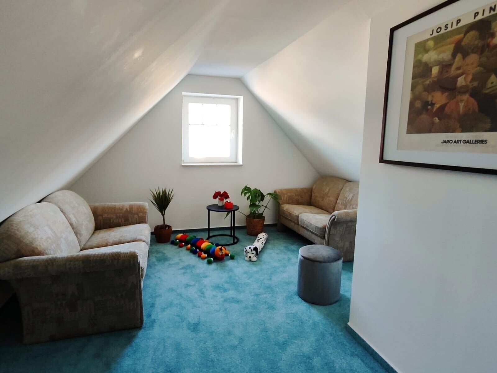 Ein gemütliches Dachzimmer mit zwei beigen Sofas, einem kleinen runden Tisch und einem Fenster.