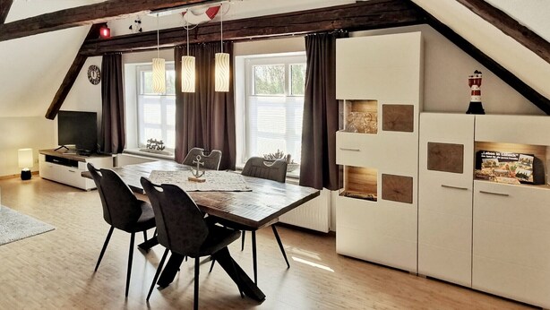 A dining area with a wooden table, black chairs, and a white cabinet with glassware.