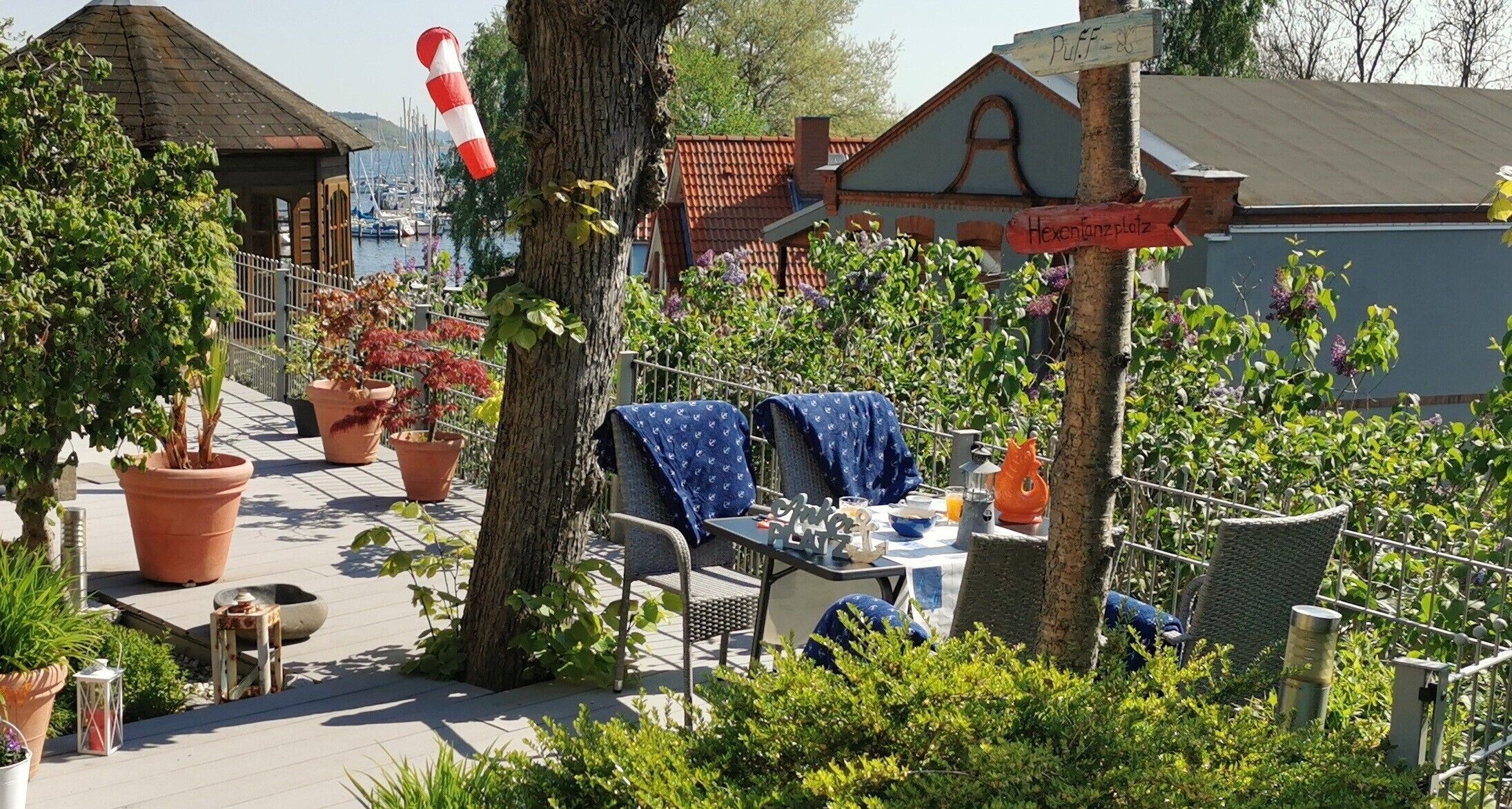 Eine Terrassenfläche mit Sitzgelegenheiten im Freien, Kübelpflanzen und Blick auf das Meer.
