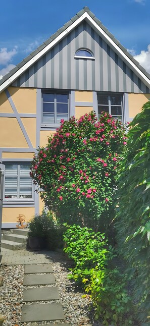 A house with a sloped roof, a window, and a garden with pink flowers.