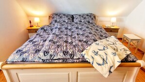 A bed with a heart-patterned duvet, two bedside lamps, a small nightstand, and a wooden headboard.