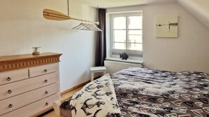 Een slaapkamer met een bed, een dressoir, een raam en een wandlamp.