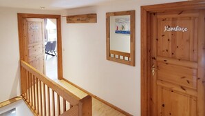 A wooden staircase with a railing, a door labeled 'Kombüse,' and a painting of sailboats on the wall.