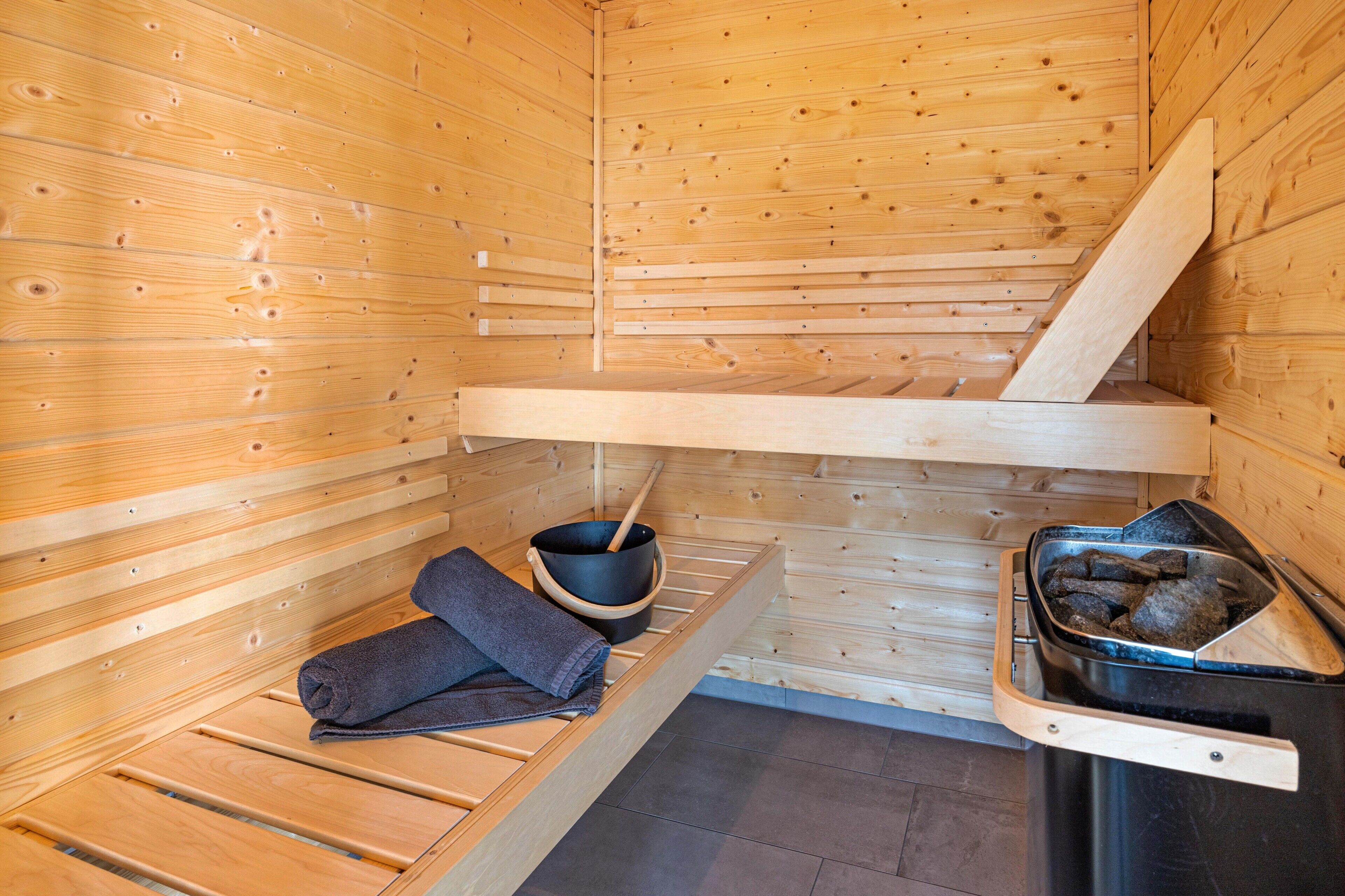 A sauna with wooden benches, a black bucket, and a metal container with stones.